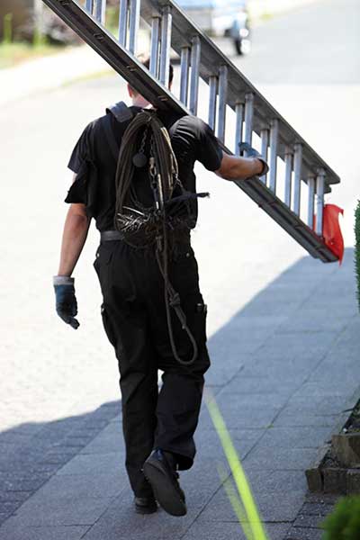 Chimney Sweep dressed in black carrying a large metal ladder