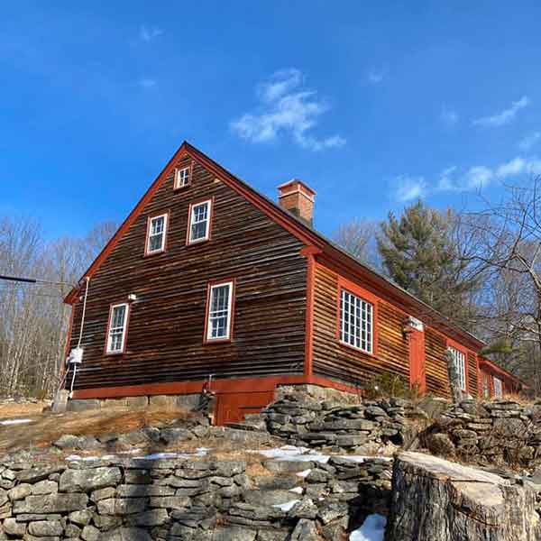 Large cabin style home on small hill with rocks surrounding it. A sunny day with Blue sky
